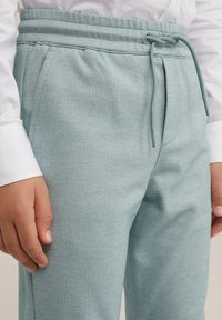 Světlé tyrkysové tepláky vyrobené z texturované tkaniny, s elastickým páskem na šňůrku a bočními kapsami.