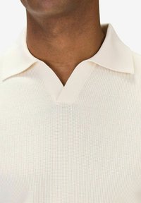 Stickad polo tröja i ljusbeige, med V-ringning, texturerad tyg med ribbat krage och minimala sömnadsdetaljer.