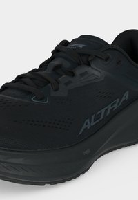 Μαύρο αθλητικό παπούτσι Altra με πλέγμα στην επιφάνεια, δέσιμο με κορδόνια και λογότυπο στο πλάι και στη γλώσσα, πάνω σε λευκό φόντο.