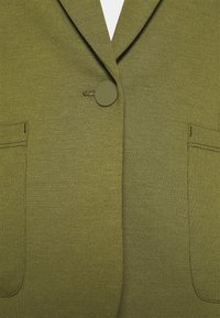 Blazer verde oliva con finitura testurizzata, chiusura con un solo bottone e due tasche frontali. Presenta un design con rever a punta.
