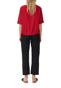 Haut rouge à manches courtes avec une coupe ample et un ourlet froncé, associé à un pantalon noir taille haute de longueur crop et des sandales plates marron.