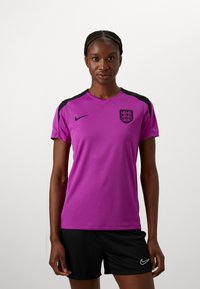 Pink athletic t-shirt with black accents, short sleeves, round neckline, featuring a logo on the chest. Worn with black shorts.