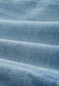 Jasnoniebieska denimowa tkanina z widocznym wzorem splotu i lekką teksturą, z widocznymi zagnieceniami i fałdami, które dodają głębi.