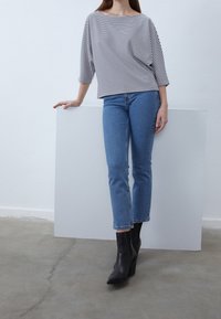 Randig, löst sittande topp i svart och vitt, i kombination med ljusblå, korta jeans och stiliga svarta ankelstövlar. Minimalistisk design, avslappnad stil.