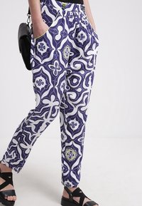 Lila- och vita mönstrade byxor med elastisk midja, sidfickor och svarta detaljer. Materialet verkar lätt och mjukt.