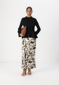 Black, textured long-sleeve top with gathered details, paired with a flowing, cream skirt with black and brown abstract patterns. Brown clutch and light heels.