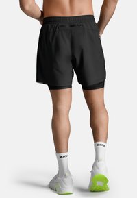 Zwarte sportshorts met een aansluitende binnenvoering, een elastische tailleband en een klein zakdetail. Gecombineerd met witte schoenen met neon groene accenten.