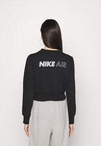 Felpa nera corta con "NIKE AIR" ricamato in bianco sul retro. Presenta maniche lunghe e collo rotondo. Abbinata a pantaloni della tuta grigi.