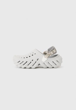 White rubber clogs with a textured, ridged sole, side ventilation holes, and a grey adjustable heel strap.