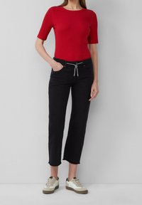 Top ajustado rojo de manga corta combinado con jeans negros de tiro alto con cordón y dobladillo deshilachado, usado con zapatillas beige y blancas.