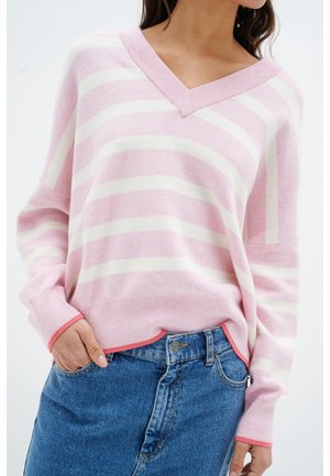 Gestreifter Pullover in Pink und Weiß mit V-Ausschnitt und langen Ärmeln, versehen mit gerippten Bündchen und einem Saum mit korallfarbener Akzentuierung. Getragen über einem Jeansrock.