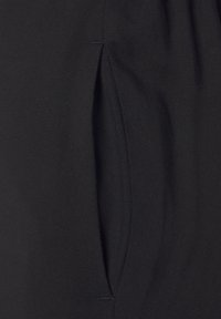 Černá tkanina s texturovanou vazbou, s bočním švem a skrytým kapsou, navržená pro pohodlí a funkčnost.