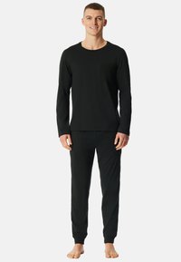 Zwarte lange mouwen top en bijpassende broek van zachte stof. De top heeft een tekstuurzakje op de linkerkant van de borst.
