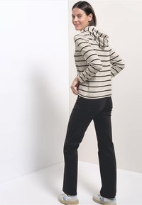 Beżowy, paskowany hoodie z kapturem na sznurku, w zestawieniu z czarnymi spodniami i jasnymi sneakersami. Gładki materiał i dopasowany krój.