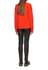 Roter gestrickter Pullover mit tief angesetzten Schultern, kombiniert mit eng anliegenden schwarzen Lederhosen. Das Modell trägt dunkelgrüne Stiefel mit dickem Absatz.