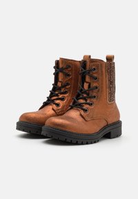 Botas de tobillo de color bronce hechas de un material metálico con cordones negros, un panel lateral texturizado y una suela negra robusta.