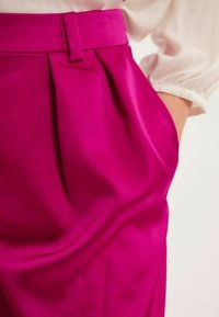 Pantalons plissés fuchsia en tissu lisse avec une taille ajustée. Poches latérales visibles, créant une silhouette détendue et fluide.