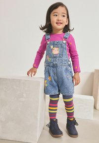 Pantalones de mezclilla con parches coloridos, de longitud corta, combinados con una camisa de manga larga rosa, leggings a rayas y botas navy con borlas.