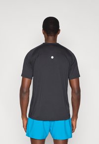 Μαύρο αθλητικό t-shirt με κοντά μανίκια και υφασμάτινες λεπτομέρειες στους ώμους, με μικρό ανακλαστικό λογότυπο στην πλάτη. Συνδυάζεται με μπλε σορτς.