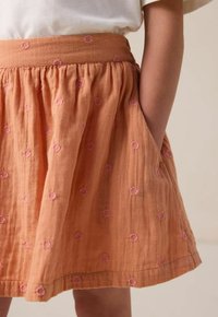 Oranger Baumwollrock mit gerafftem Bund, der mit pinkfarbenen bestickten Blumenmustern verziert ist, und seitlichen Taschen. Weicher, strukturierter Stoff.