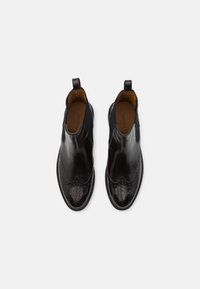 Bottines noires en cuir avec des détails en brogue, des panneaux élastiques sur les côtés et des languettes de tirage. Texture lisse et forme de orteil arrondie.