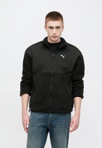 Giacca in pile nero con chiusura a zip, maniche dalla texture morbida e sezione superiore solida, con logo del marchio bianco sul petto.