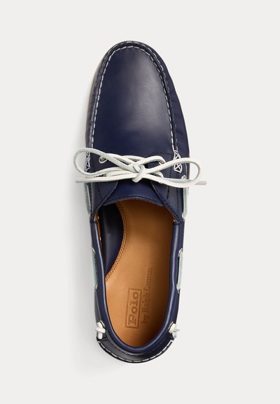 Mocassino da uomo in pelle blu navy con lacci bianchi annodati a fiocco e sottopiede in pelle color cuoio con timbro Polo by Ralph Lauren.