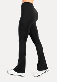 Musta korkeavyötäröiset legginsit, joissa levenevät lahkeet ja joustava materiaali, yhdistettynä valkoisiin urheilukengiin.