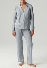 Jasnoszary zestaw piżamowy z długim rękawem, zapinany na guziki, z kieszenią oraz dopasowanymi spodniami o prostym kroju, wykonany z miękkiego materiału.
