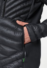 La giacca nera isolata presenta un design a rombi, una tasca con cerniera, una texture liscia e un'etichetta del logo ben visibile vicino all'orlo.