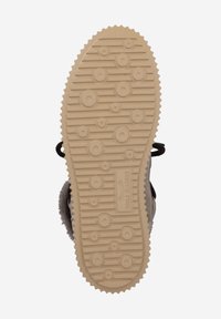 Semelle de chaussure avec une surface en caoutchouc texturé beige, présentant des motifs circulaires et des crêtes pour l'adhérence. Lacets noirs attachés.