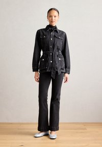Giacca in denim nera con vita regolabile, dotata di due tasche sul petto, chiuse con bottoni argentati. Abbinata a jeans neri a zampa d'elefante coordinati.