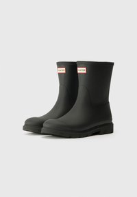 Black rubber rain boots with a rounded toe, textured sole, and red-accented logo at the top. Smooth finish and mid-calf height.