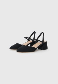 Mustat slingback-korkokengät, joissa on terävä kärki, valmistettu pehmeästä kankaasta. Sisältää paksun kantapään ja ristikkäiset hihnat lisätuennaksi.