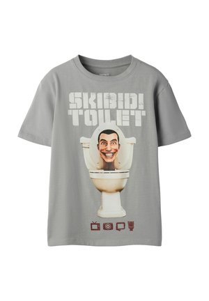 T-shirt gris à manches courtes avec le texte "SKIBIDI TOILET", une tête de dessin animé souriante dans une cuvette de toilettes et quatre petites icônes marron en dessous.