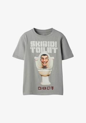 Grå T-shirt med korte ærmer med teksten "SKIBIDI TOILET", et smilende tegneseriehoved inde i en toiletkumme og fire små brune ikoner nedenunder.