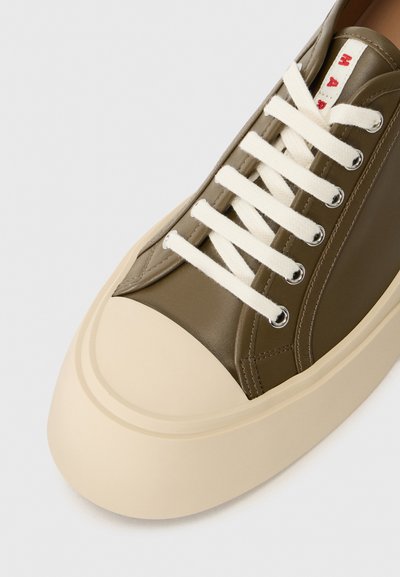 Olive green sneaker with a white rubber sole and laces, featuring subtle stitching details and a rounded toe cap.