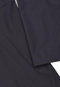 Granatowa kurtka przeciwdeszczowa z detalami ukazującymi gładki materiał, proste krawędzie oraz boczną kieszeń z precyzyjnym przeszyciem. Charakteryzuje się minimalistycznym designem.