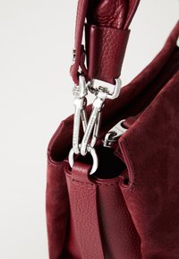 Burgundy handbag featuring leather and suede materials, silver hardware, and a zipper closure with detachable strap detail.