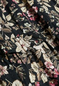 Tissu noir avec un motif floral comportant des fleurs roses, crème et vertes. La texture semble douce avec des plis et des volants visibles.