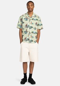 Kortærmet grøn skjorte med et fantasifuldt print af udendørsscener, parret med hvide shorts og sorte sko. Casual, afslappet pasform.