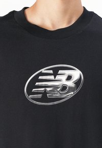 T-shirt en coton noir présentant un grand graphique logo 3D argenté sur la poitrine. L'encolure est de style classique à col rond.