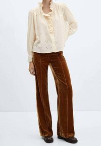 Blusa crema con scollo a volant e dettagli ricamati, abbinata a pantaloni a zampa in velluto marrone con accenti in piping laterali.