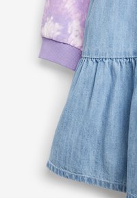 Robe en denim avec une jupe bleue et un haut à manches longues tie-dye lilas. Elle présente une taille froncée et des poignets côtelés sur les manches.