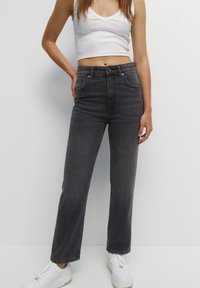 Jeans de mezclilla negros de tiro alto con corte recto, cinco bolsillos y sutiles acentos de hardware, combinados con un crop top blanco ajustado.