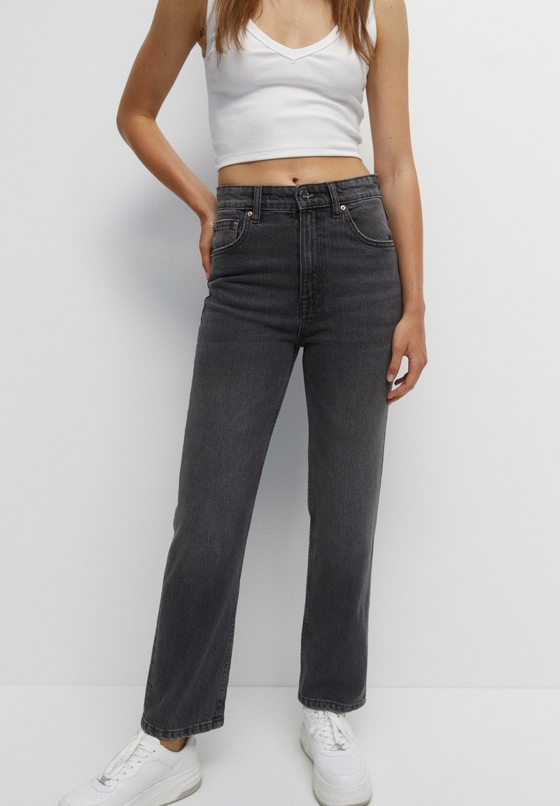 Jeans de mezclilla negros de tiro alto con corte recto, cinco bolsillos y sutiles acentos de hardware, combinados con un crop top blanco ajustado.