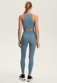 Světle modrý atletický crop top a legíny s vysokým pasem, bezešvý design, měkká textura, doplněné černými sportovními botami, pohled zezadu.