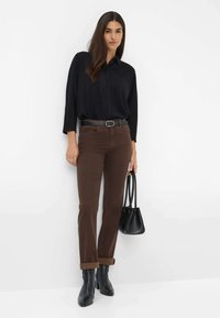 Blusa nera con bottoni, jeans dritti marroni, cintura nera, stivaletti neri alla caviglia e una piccola borsa nera. Tessuto morbido e dettagli con maniche arrotolate.