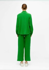 Chemise verte ample à texture et pantalon large, avec un col et des manches longues. Complet avec des chaussures légères.