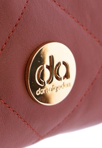 Bolso de mano de cuero rojo con patrón de diamantes, que presenta un herraje circular dorado grabado con el logo y detalles de costura en naranja.